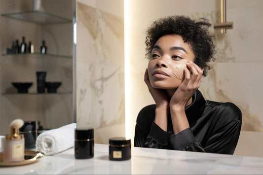 A woman stands in a bathroom, looking into a mirror while holding a bottle of face cream