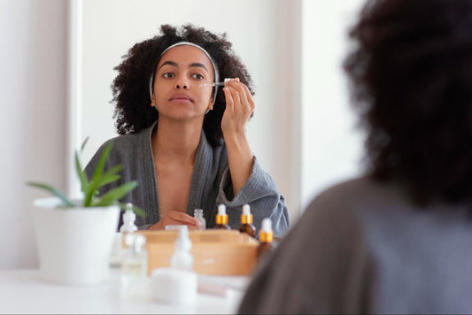 A woman applies makeup while gazing into a mirror, focusing on her reflection and enhancing her features.