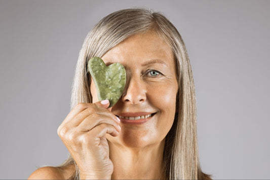 A woman holds a green leaf in her hand, showcasing its texture and vibrant color against a blurred background.