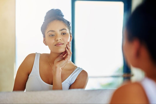 A woman gazes into a mirror, examining her face with a thoughtful expression.