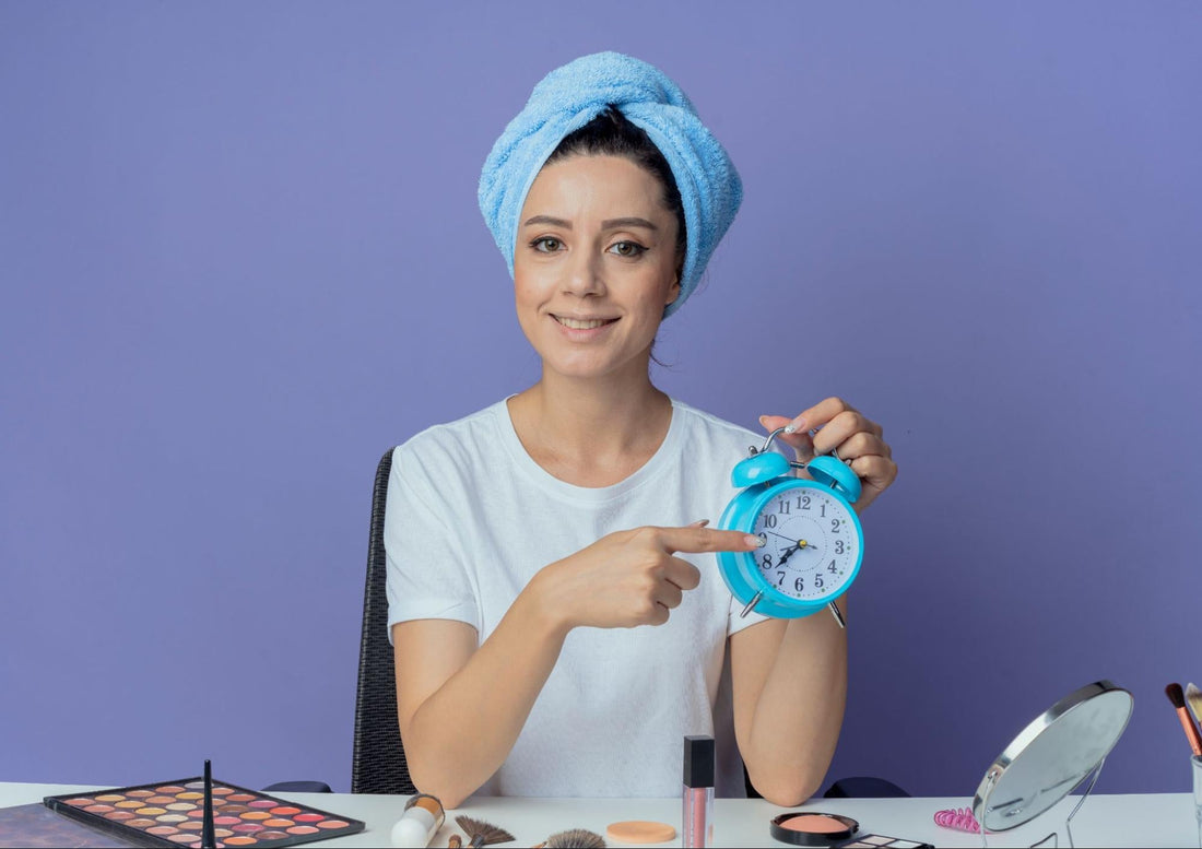 Woman with a towel on her head, holding an alarm clock, looking surprised in a bright, cozy room.