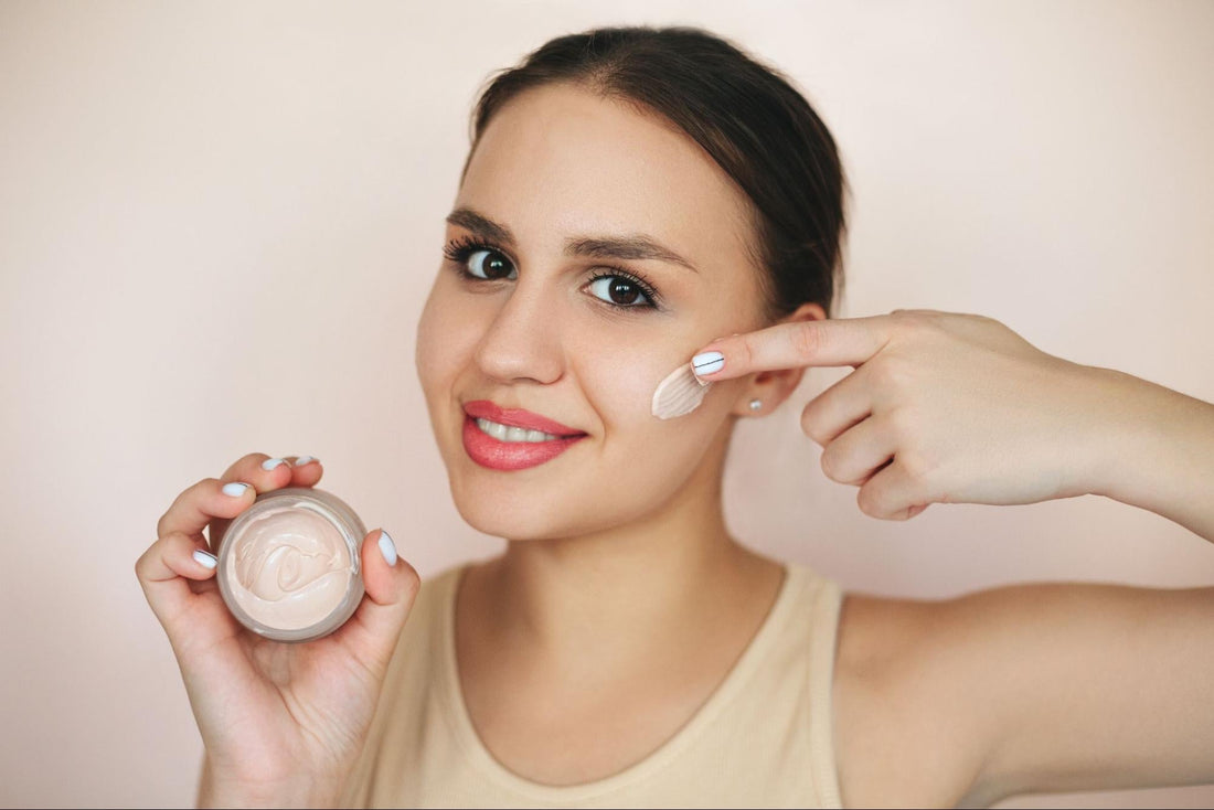 A woman holding a tube of cream foundation, showcasing its color and texture for makeup application.